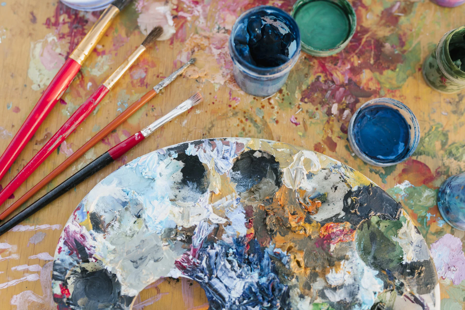 Paleta con pinturas al óleo, pinceles y botes de color sobre una mesa de trabajo artística