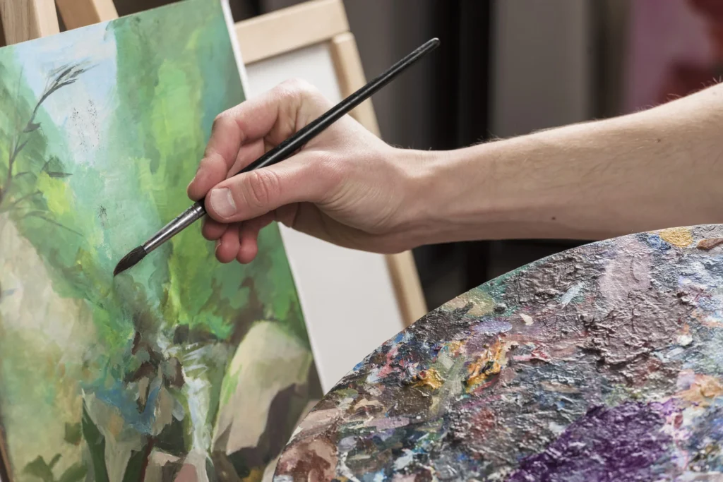 Artista pintando un cuadro al óleo sobre lienzo con pincel y paleta de colores